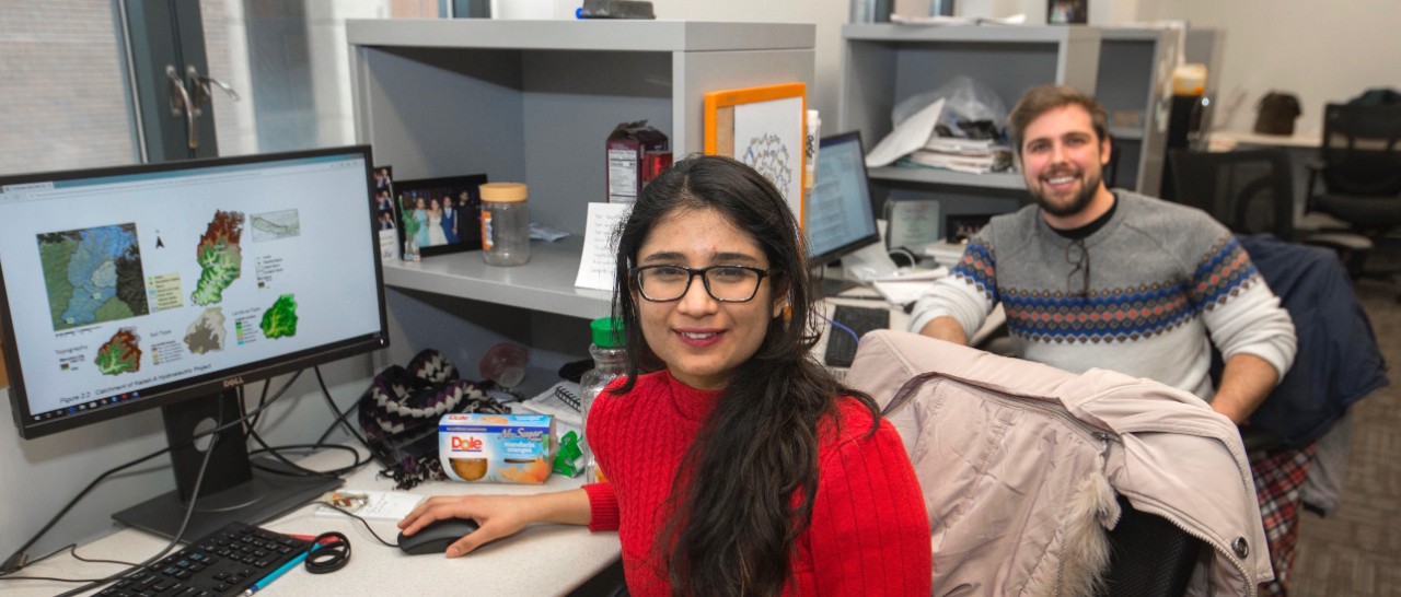 Two UC engineering students sit at their desks in front of computer terminals .