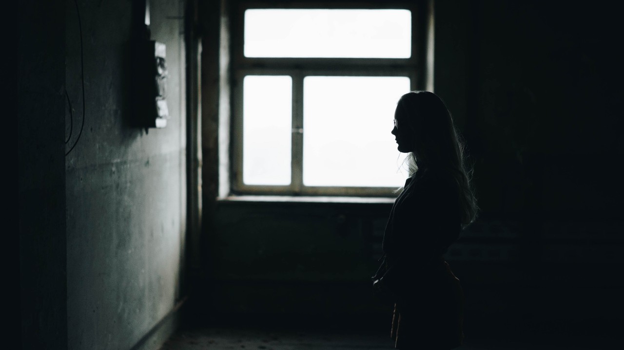 A silhouette of a woman backlit by a window in a dark room