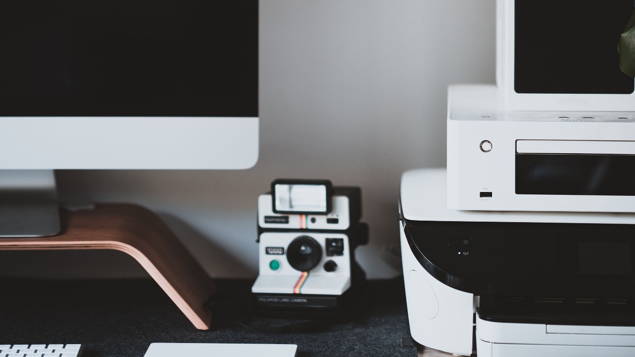 Printer setup on desk next to desktop computer and camera.