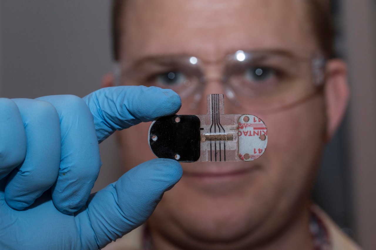 UC graduate Adam Hauke holds up a sweat sensor to his face in UC's Novel Device Lab. 