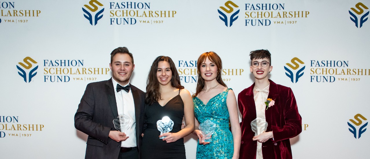 Four well-dressed students stand in front of a Fashion Scholarship Fund background.