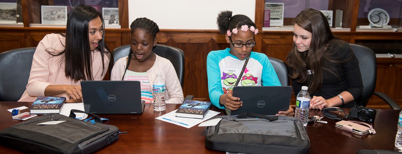 Two medical students shown with young mentees using laptops at UC College of Medicine.