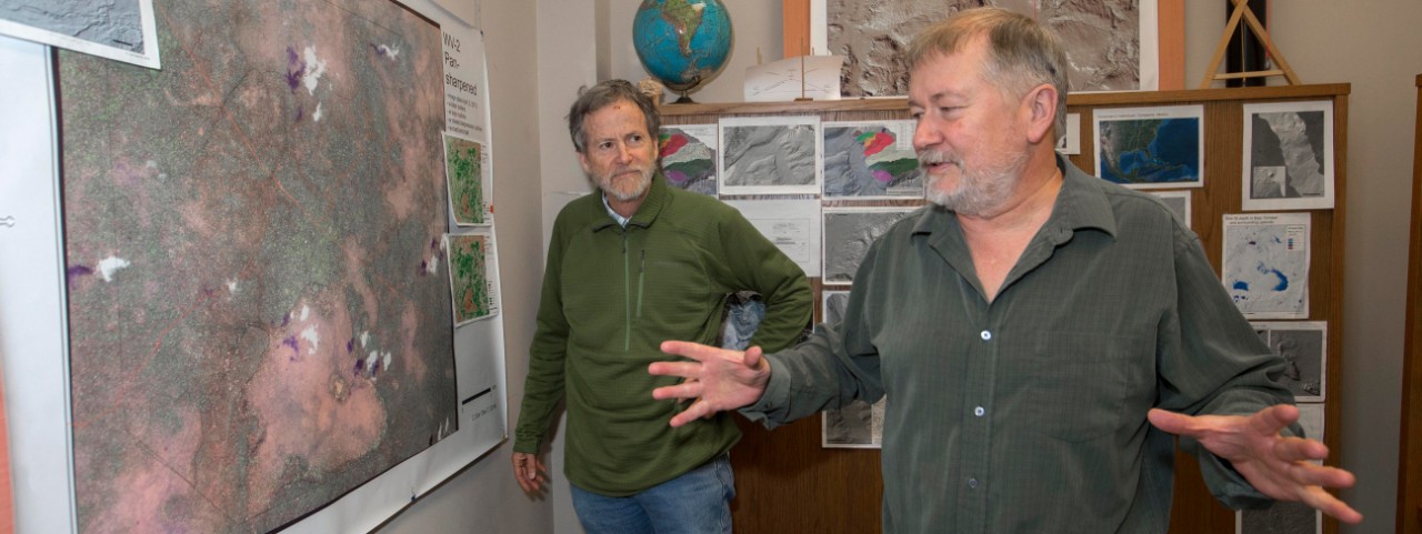 UC geography professors Nicholas Dunning and Christopher Carr stand at a large satellite map of their study area in the Yucatan Peninsula in Carr's office.