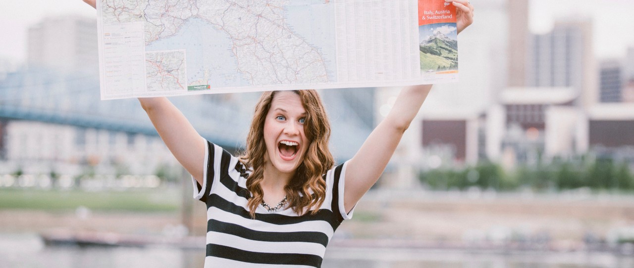 UC student Kendall Cappel holds up a map of Austria while she stands in front of buildings in Vienna.