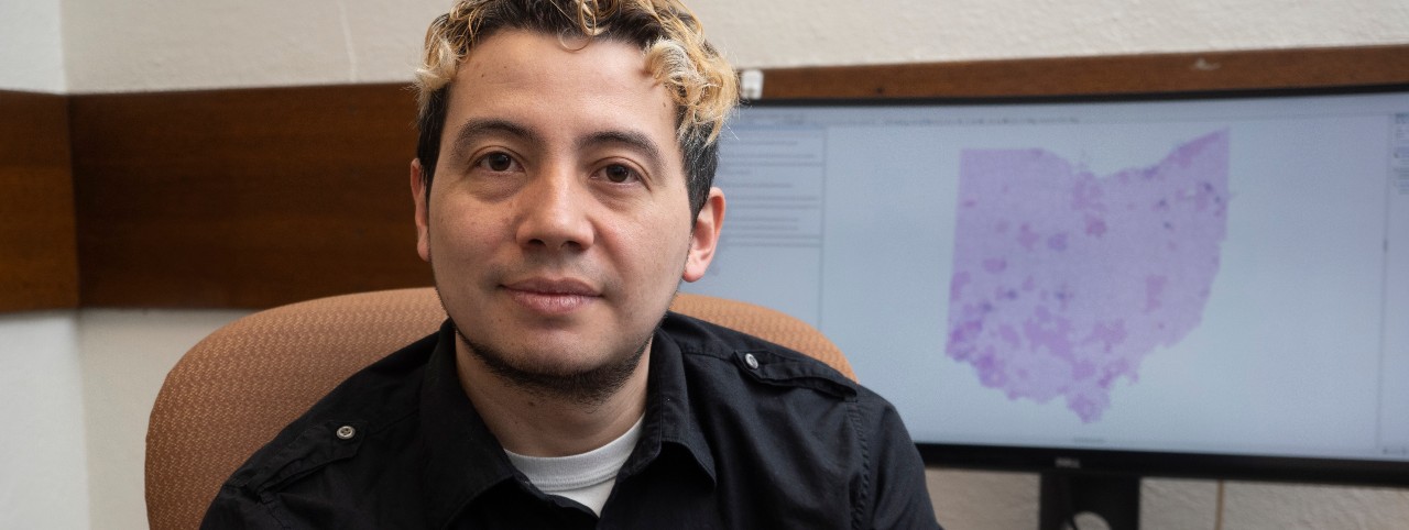 UC student Andres Hernandez poses in front of a computer screen with his Ohio opiate map. 