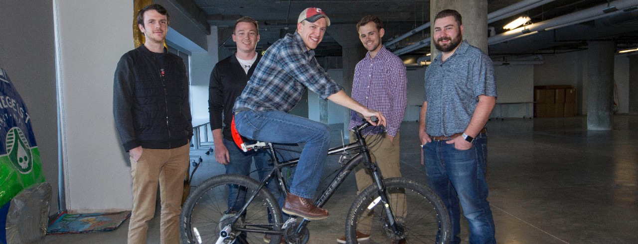 UC mechanical engineers stand around a rider who is testing a new brake on a bicycle mounted on a stationary rack.