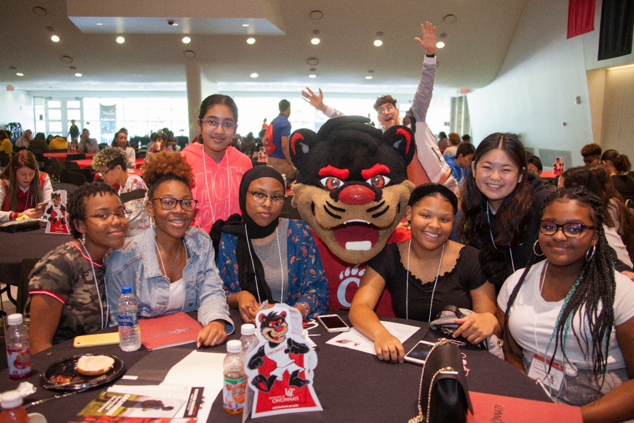 a group pf students sit at a table with the Bearcats mascot