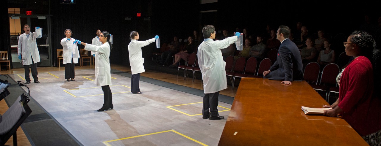 Scene from Blind Injustice opera shows actors in lab coats holding test kits