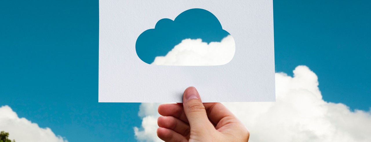 Hand holding a card with cloud cutout; fluffy white clouds and blue sky background
