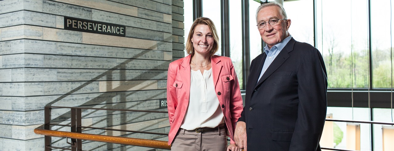 Joni Fedders and Clay Mathile posing at their organization, Aileron, by the stairwell. "Perseverance" written on wall in background.