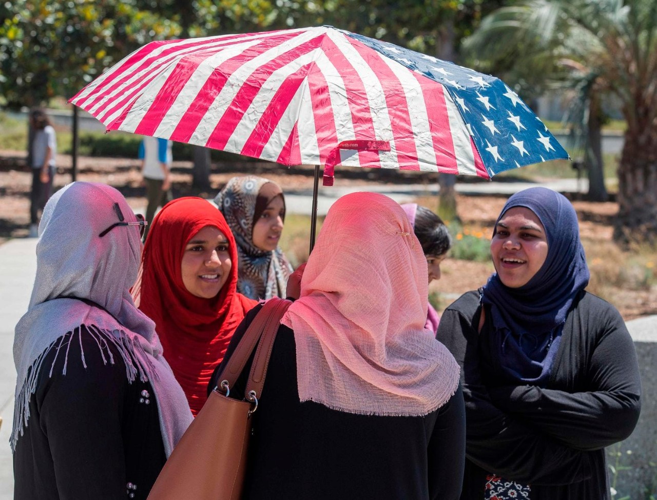 muslim women with headpieces stand below an umbrella