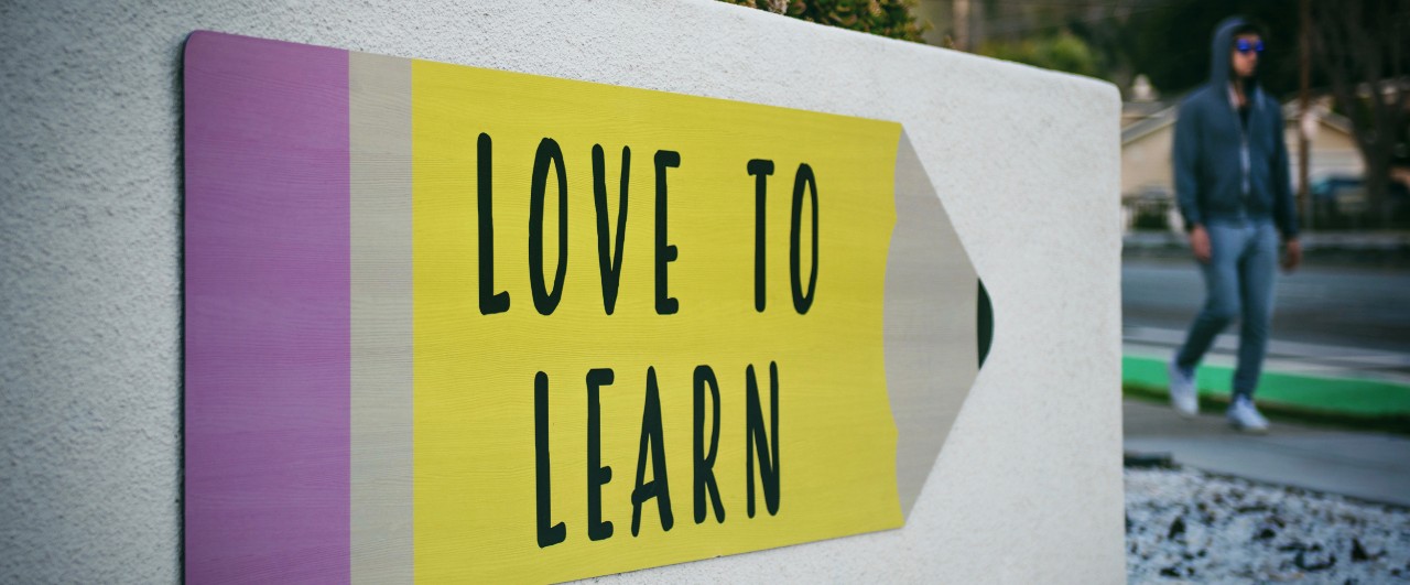 Large fence sign painted like a pencil with the words, "Love to Learn."