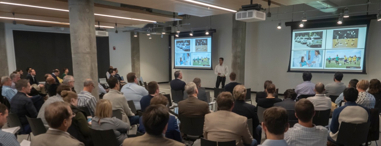 An audience gathered in a room with two large video displays in the front.