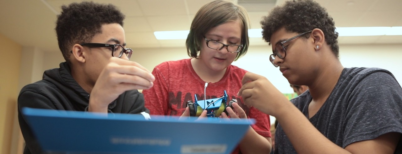 Three students collaborate on a robotics project.