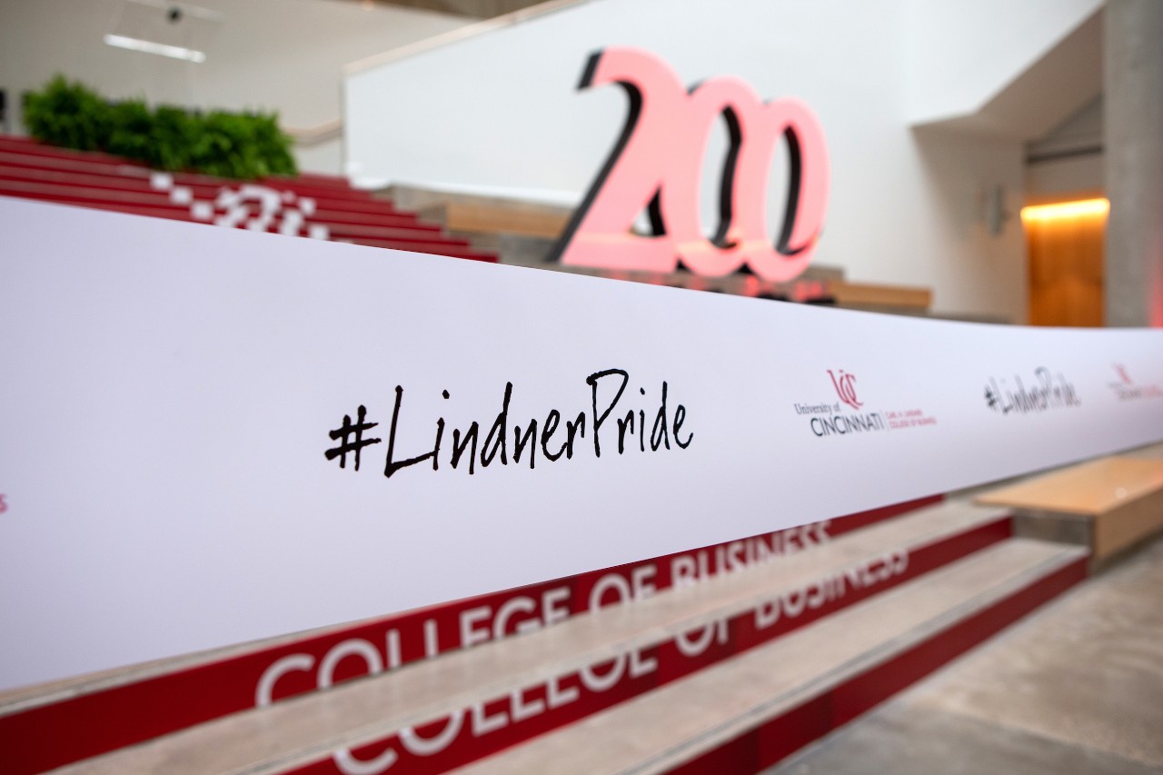 "#LindnerPride" and the UC logo appear on the ceremonial ribbon at the grand opening of the new Lindner Hall. The UC Bicentennial logo can be seen in the background
