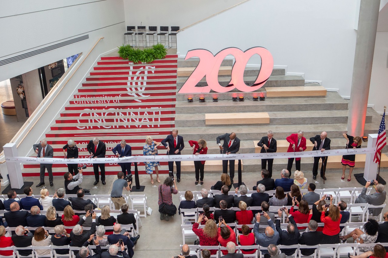 a row of people line up in a large atrium and cut a large ribbon with pairs of ceremonial scissors