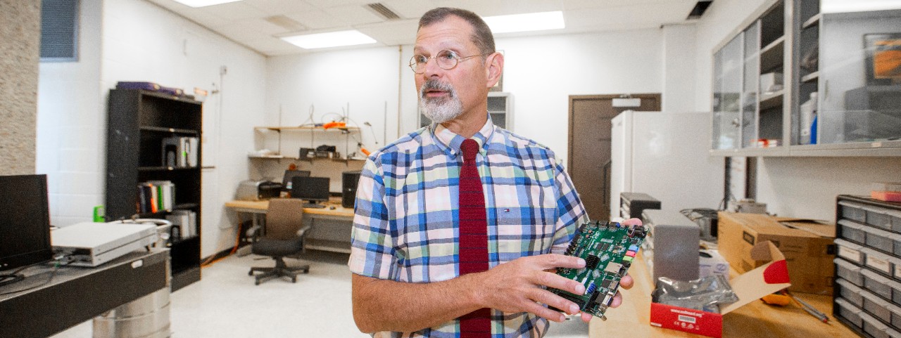 UC engineering professor John Emmert holds up a circuit board in a lab.