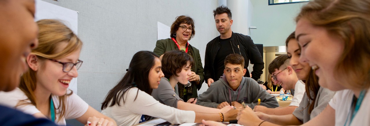 Students sit around table discussing design strategies.