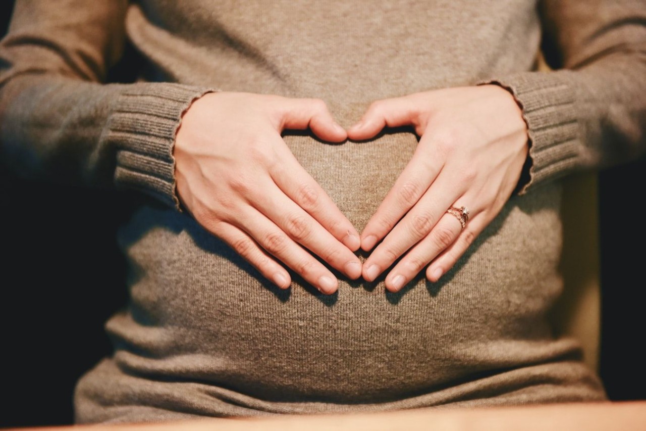 Pregnant woman makes a heart shape with her hands on her stomach