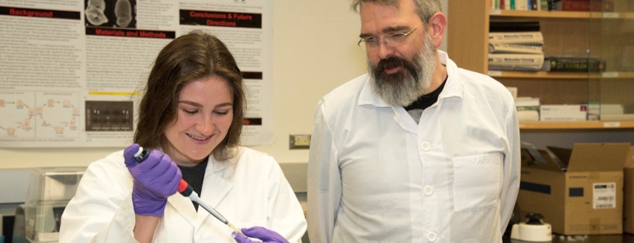 Student and professor in white coats work in a lab