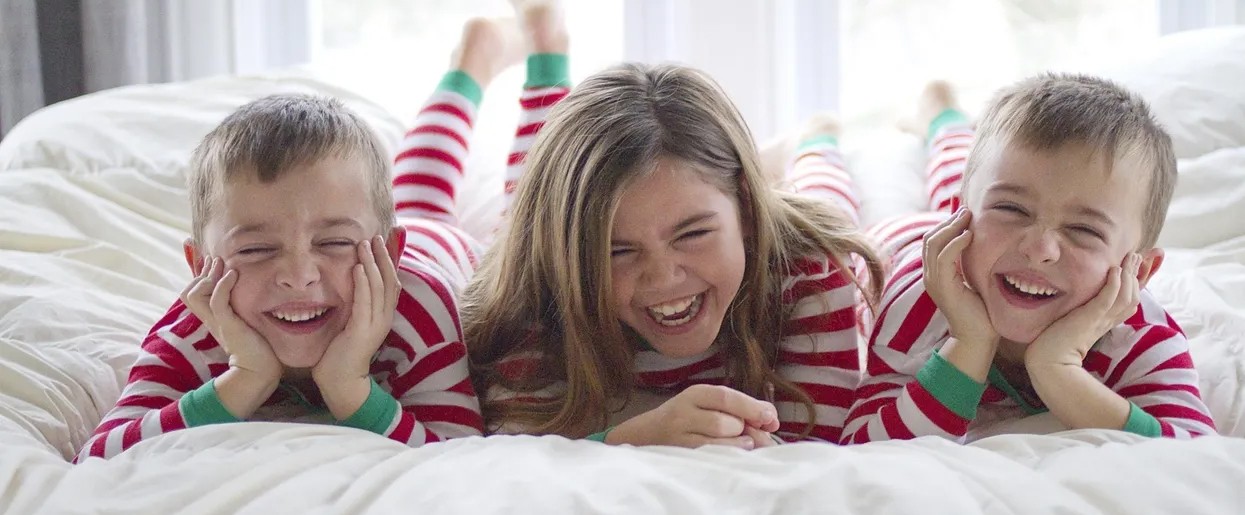 three children wearing pajamas lie on a bed