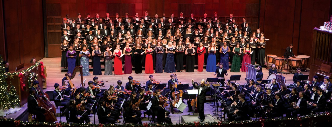 A large choir on a decorated stage with instrumentalists in the pit.
