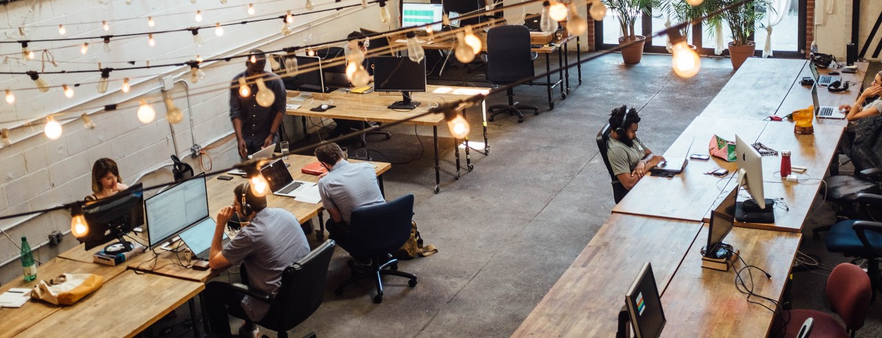 Modern office with lights hung over head and several tables and computers.