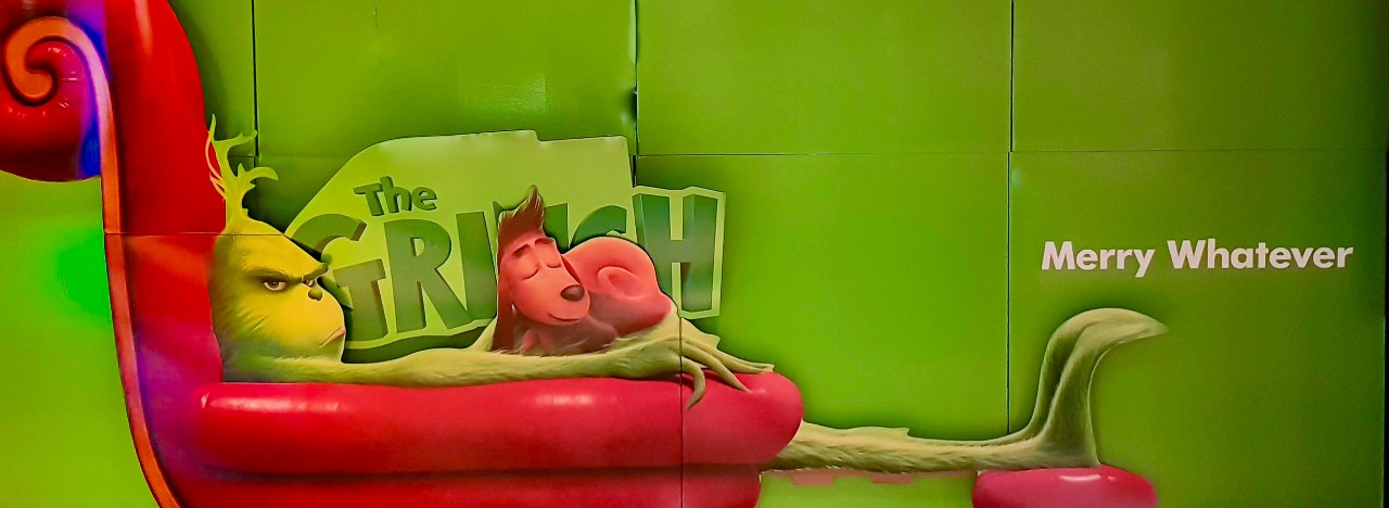 Green Grinch lays back on a long chair with his red dog on his lap.