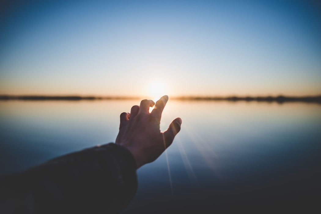 image of a hand against the backdrop of a sunset
