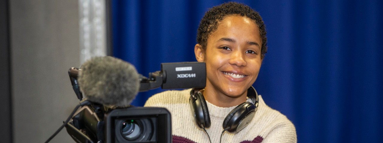 UC electronic media student Mary Williams with headphones on and operating a large video camera.