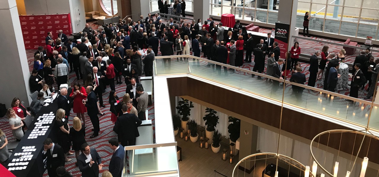 a crowd of approximately 100 people gather and mingle in an atrium for a reception