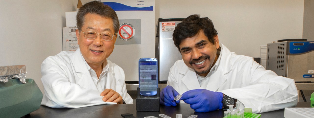 UC engineering professor Chong Ahn, left, and his graduate student Sthitodhi Ghosh pose with the lab accessory they designed for smartphones.