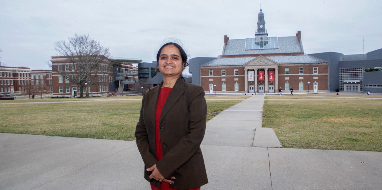Shailaja Paik standing on campus with the Next Lives Here sign behind her