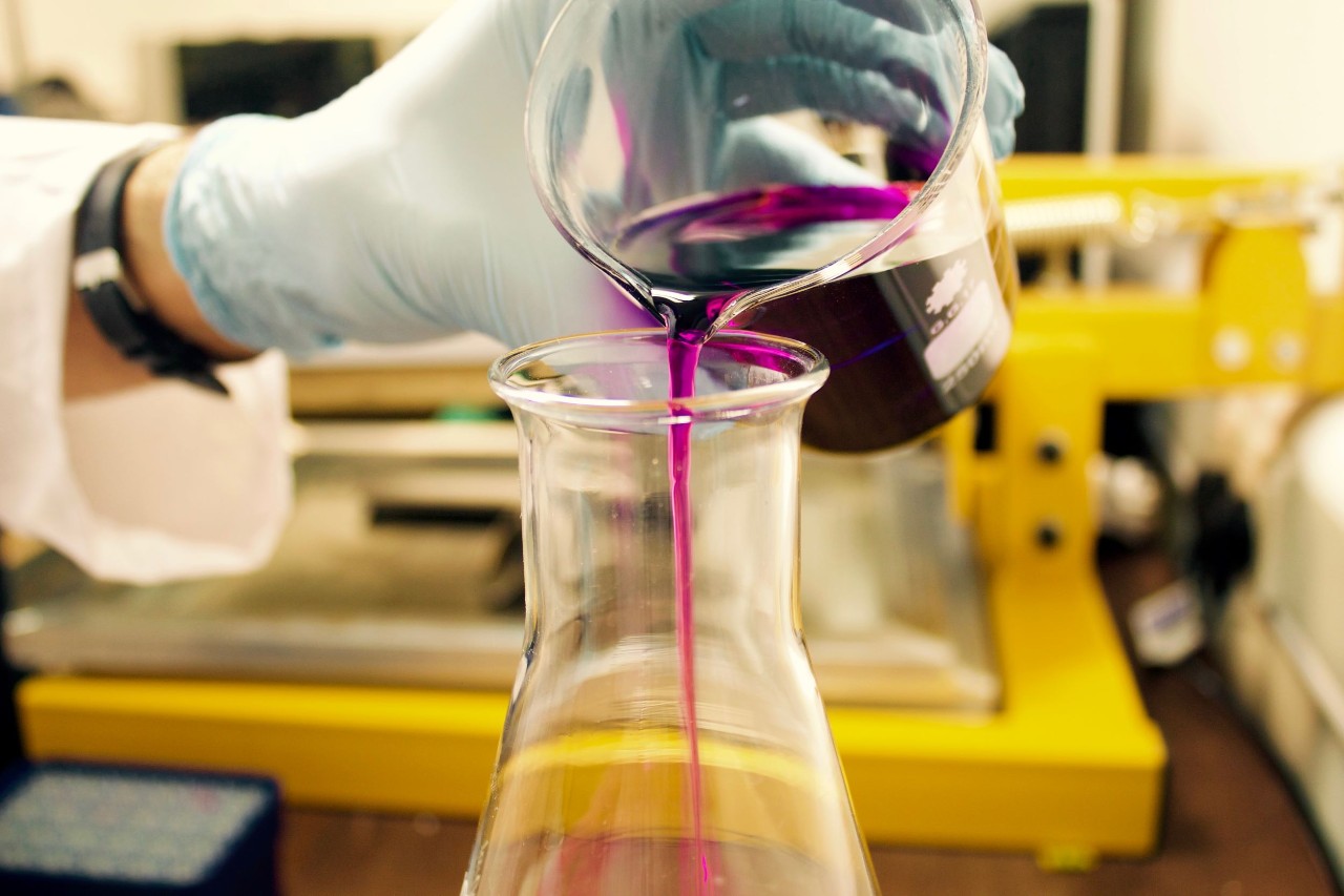 hand pouring purple liquid into a beaker 