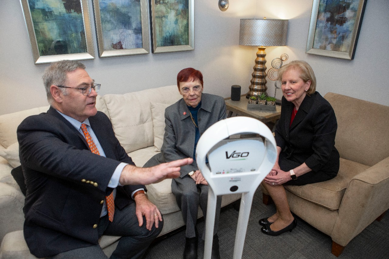 A man and two women are sitting on a couch and a chair looking at a telehealth robot.