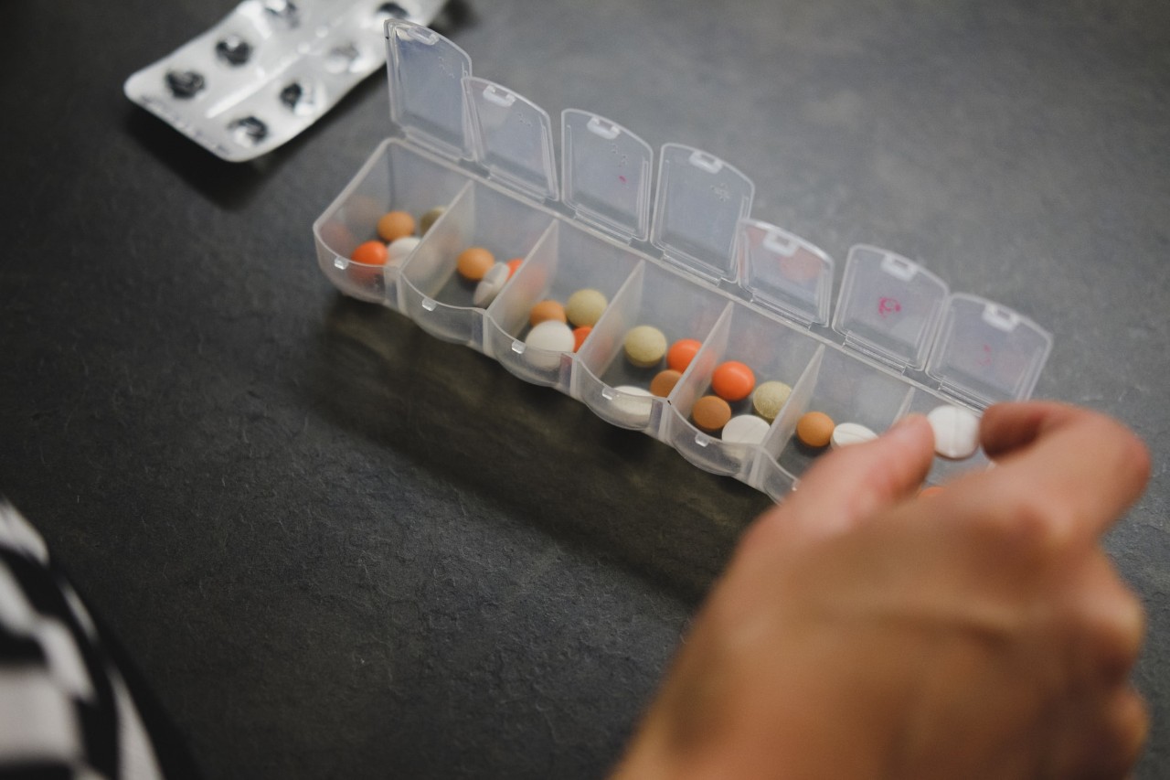 A hand puts pills into a daily reminder container.