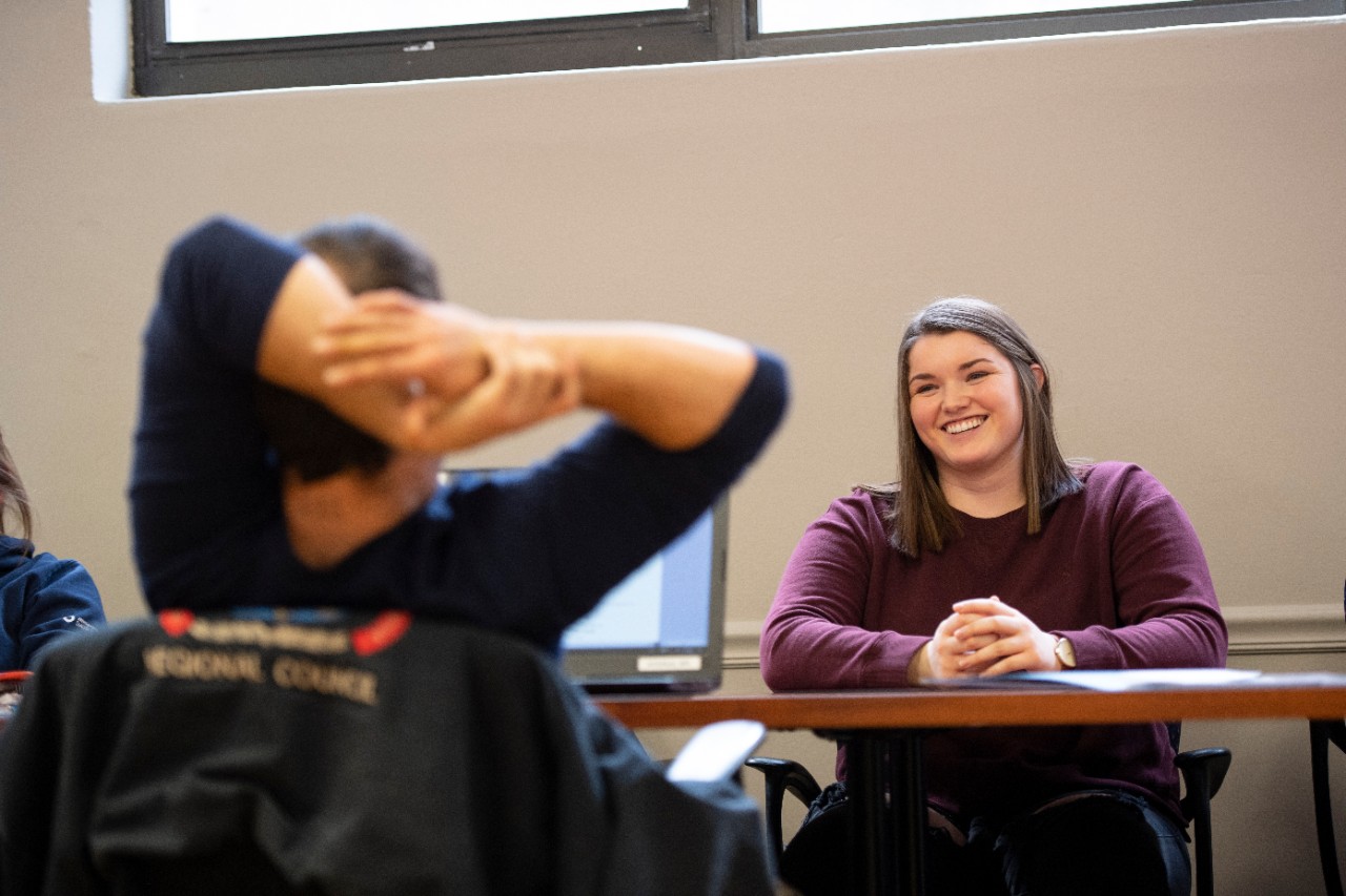 UC student Riley Jerow sits across a table from two people working on laptops.