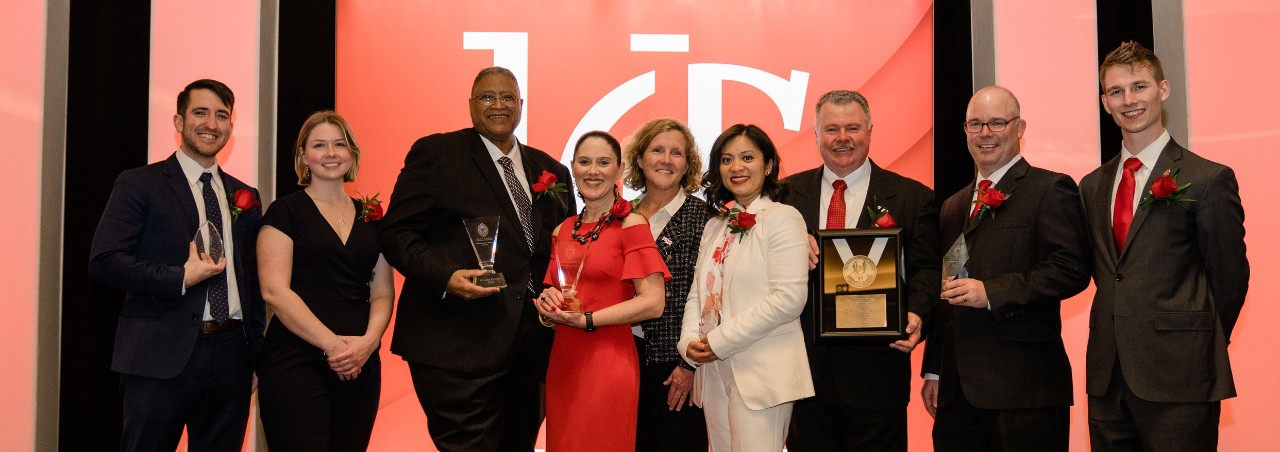 Eight awardees in business professional apparel stand with the dean of the Lindner College of Business, center on a stage in front of a UC backdrop