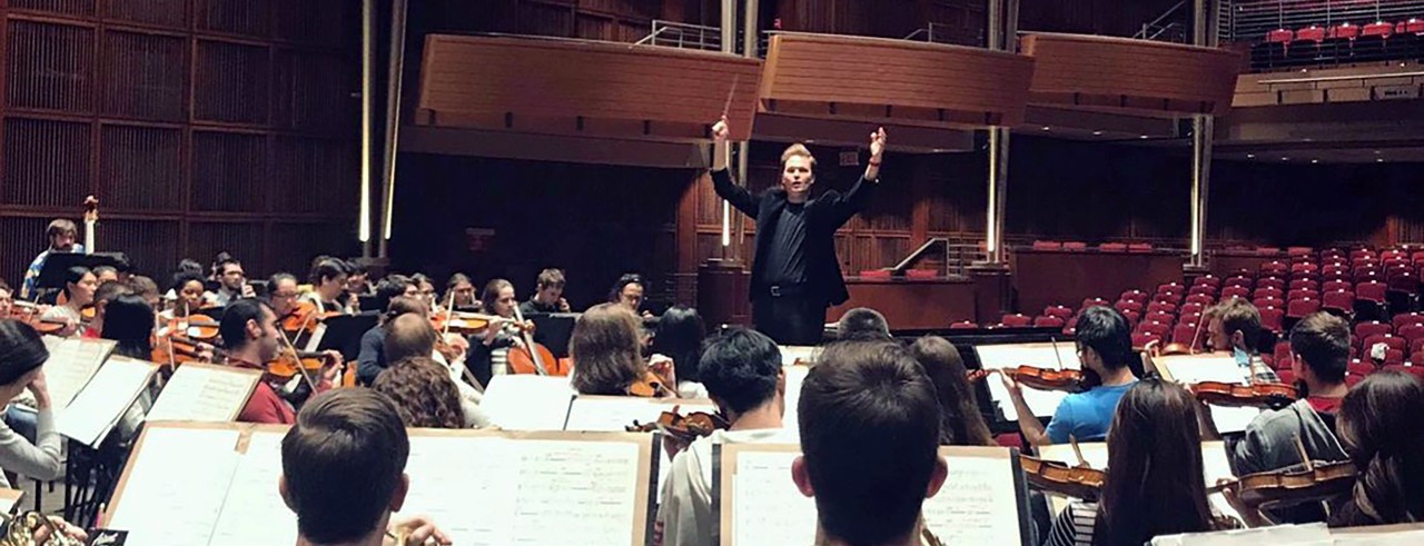 A conductor leads an orchestra on stage
