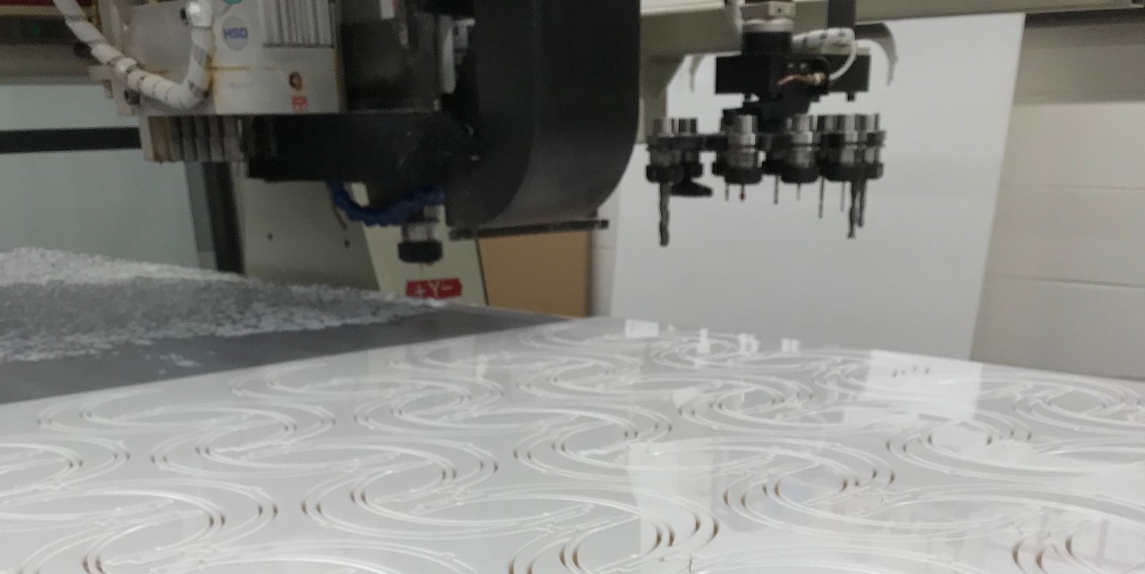A white sheet of plastic sits atop the bed of a large robotic laser cutter