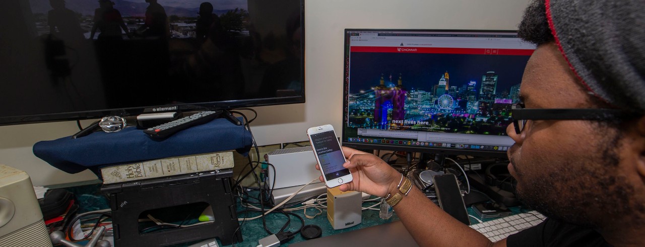 A UC student checks his phone using a voice-activated command in font of a desktop computer.