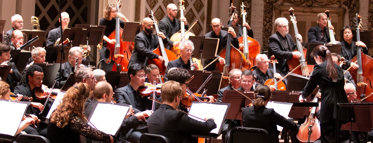 A woman conducts an orchestra on stage