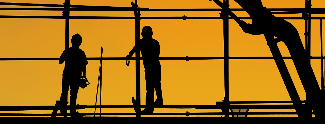 Silhoutte of two construbtion workers up high next to a machine