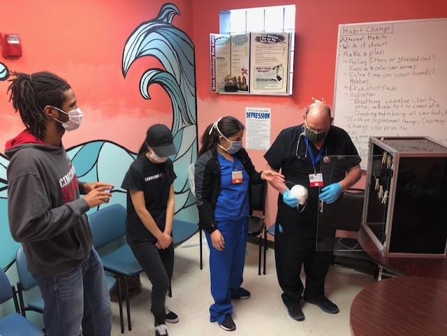 Two UC engineering students, Allison-Joy Garbo, Kellen Crosby, show their ultraviolet box to two staffers at Crossroad Health Center.