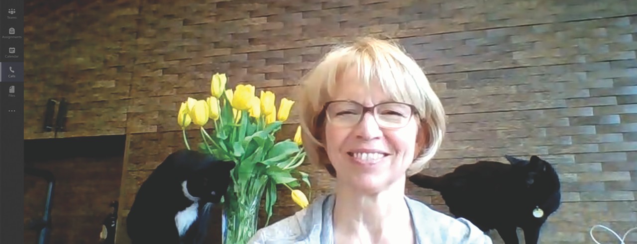Carol Butler on a video call smiling with her two cats and yellow flowers in background.