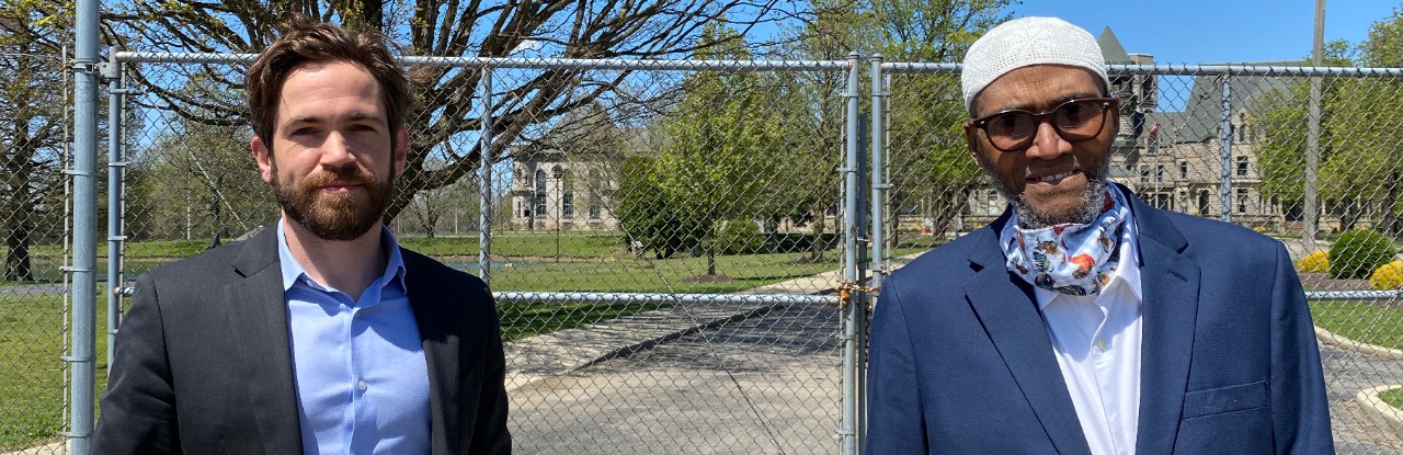 Two men in suits stand in front of a large metal gate