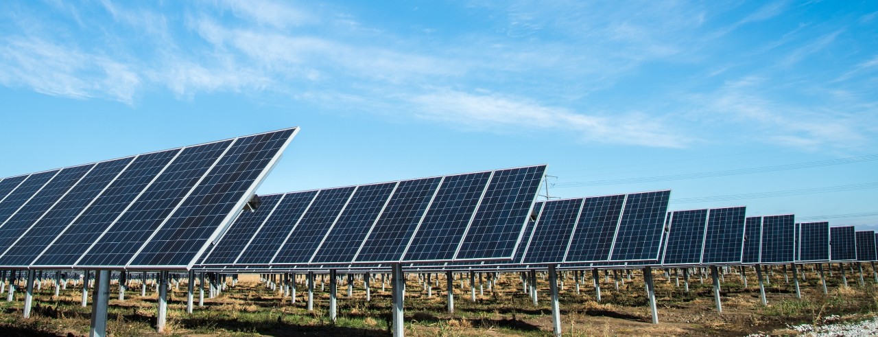 Solar panels are lined up under a blue sky with thin clouds.