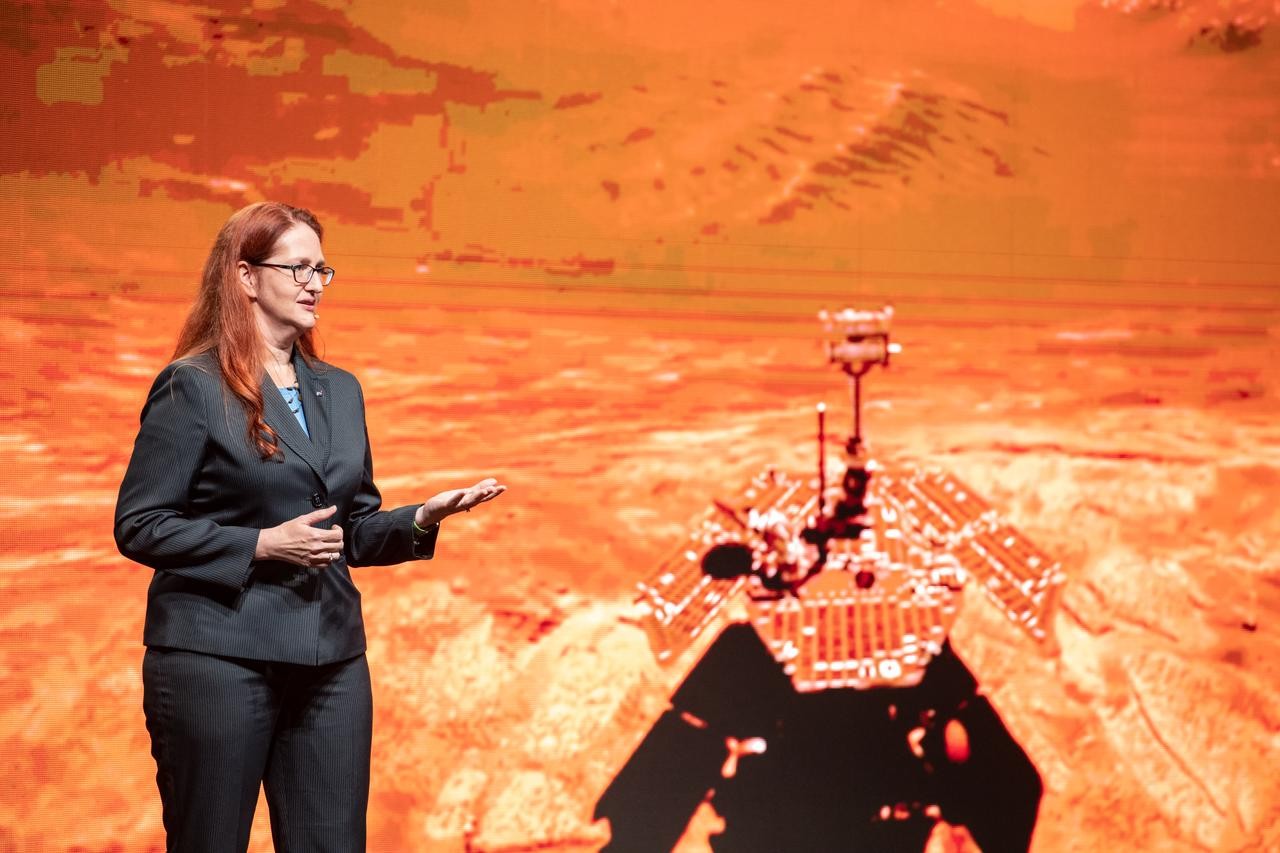 UC graduate Melissa McGuire stands on stage in front of a screen projecting the Mars rover.