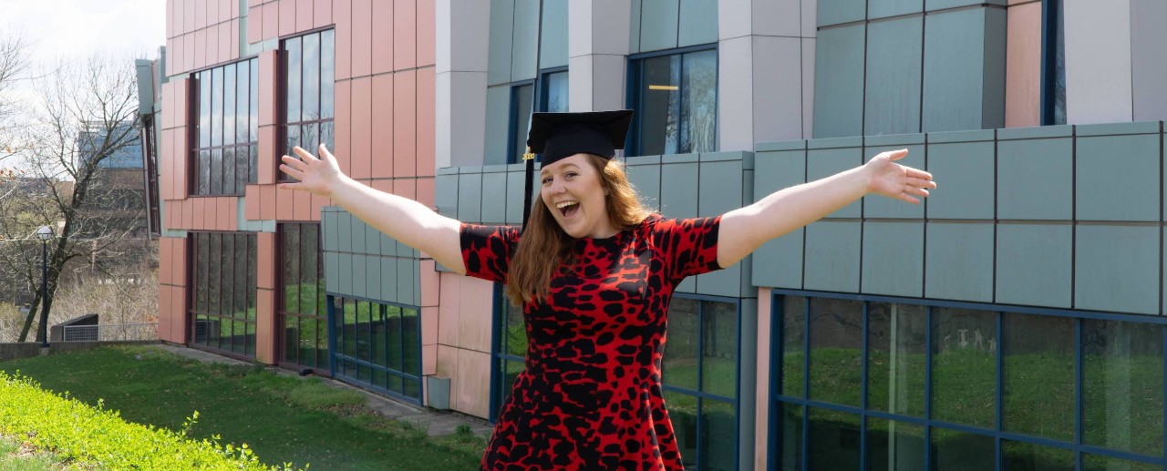 Student in graduation cap smiles with arms spread
