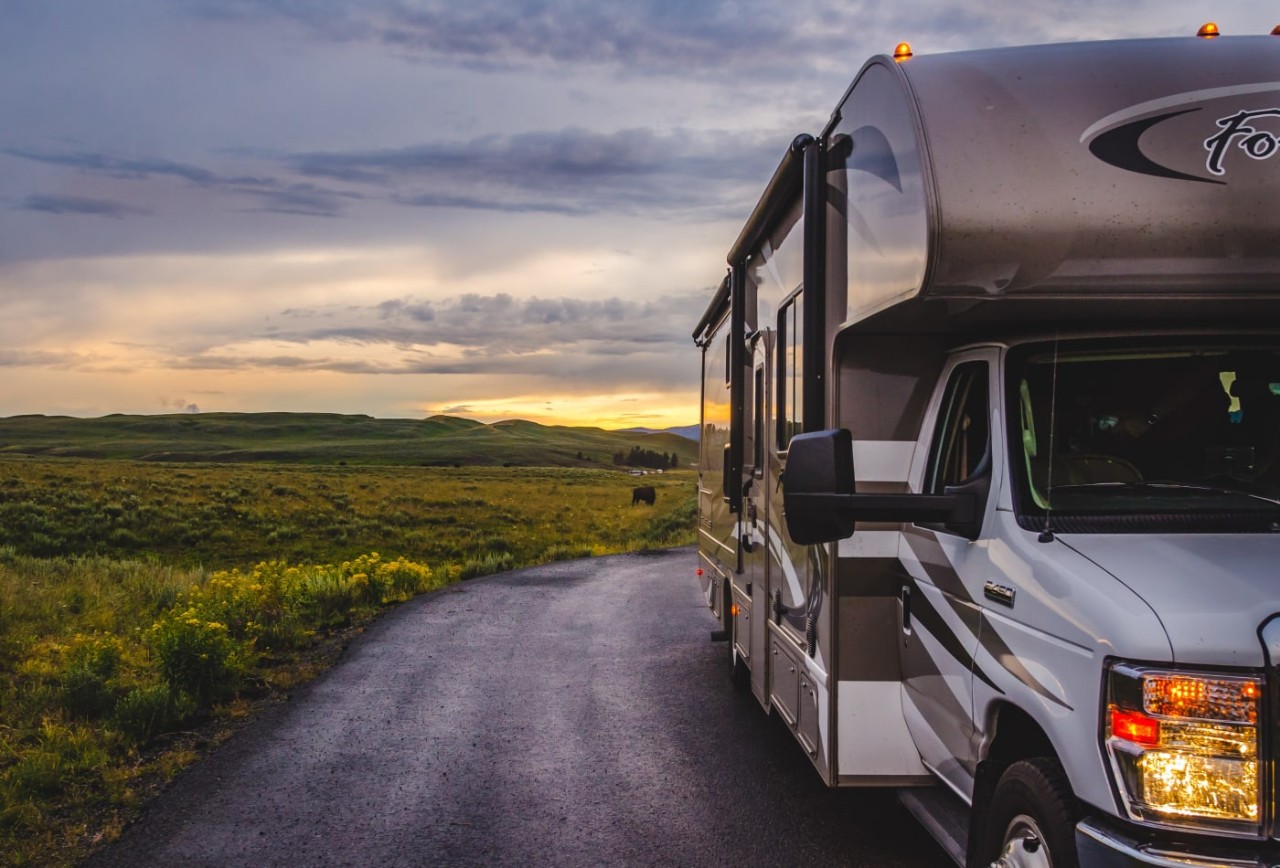 A recreational vehicle on a rural road with a sunset in the background